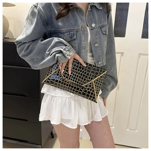 Detail of black glossy envelope clutch featuring gold geometric grid and metal trim accents