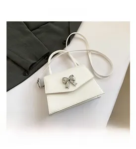 Detail view of white patent leather crossbody bag with silver bow accent on the flap