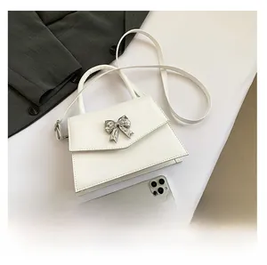 Detail of white patent leather mini bag featuring a silver metal bow and crossbody strap