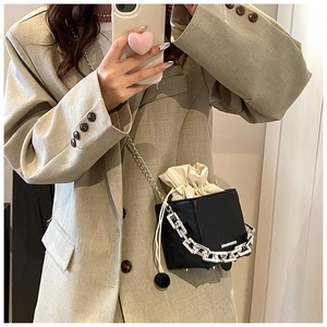 Detail of black drawstring bucket bag with thick silver chain and contrast cream lining