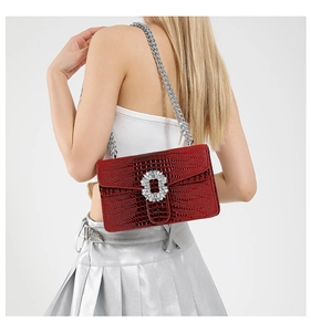 Detail of red croc-effect crossbody bag featuring a sparkling crystal buckle and silver chain