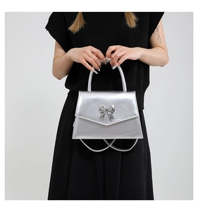 Silver patent leather handbag featuring a sparkling rhinestone bow detail and top handle