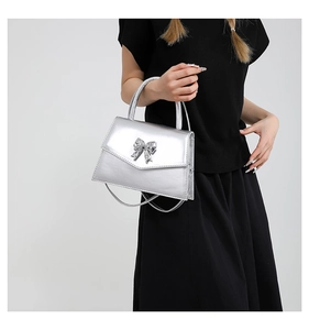 Close-up of a silver patent leather handbag featuring a metallic bow and top handle