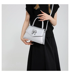 Detail of silver metallic handbag with bow ornament and elegant envelope flap design