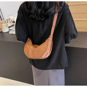 Dettaglio di una borsa a sella a mezzaluna in finta pelle marrone portata a spalla