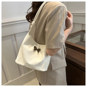 Détail du sac seau blanc cassé avec ornement papillon en métal foncé sur le côté