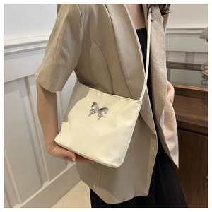 Sac à bandoulière crème élégant avec boucle papillon argentée porté par un mannequin