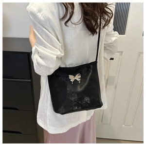 Détail d'un sac à bandoulière en similicuir noir orné d'une boucle papillon argentée