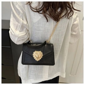 Détail d'un sac bandoulière noir avec boucle cœur dorée et bandoulière en chaîne métal