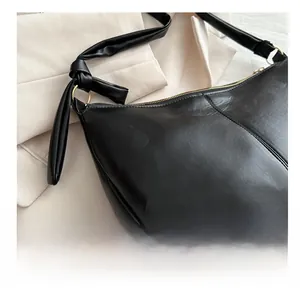 Close-up of black leather saddle bag featuring knotted strap and golden hardware