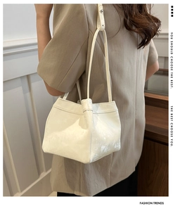 Model wearing a minimalist cream PU leather bucket bag with slim shoulder straps