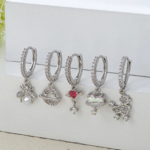 Détail de cinq boucles d'oreilles argentées avec zircon et breloques abeille, planète et cœur