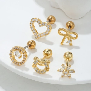 Détail de cinq clous d'oreilles dorés en zircon avec motifs cœur, nœud et flocon de neige
