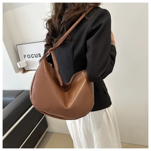 Brown faux leather crescent shoulder bag worn by model, showing minimalist hobo design