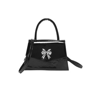 Glossy black patent leather crossbody bag with a silver bow ornament on white background