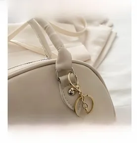 Nahaufnahme der cremefarbenen Handtasche mit Zylindergriff und goldenem Haken mit Anhänger
