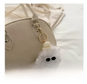 Detail eines weißen Plüsch-Anhängers mit Sonnenbrille und Mini-Hut an einer Lederhandtasche