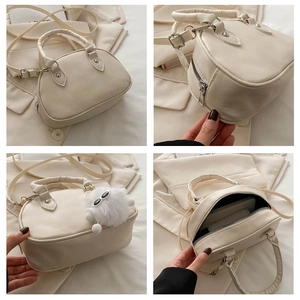 Detail der cremeweißen Boston-Tasche mit silbernen Reißverschlüssen und Plüsch-Anhänger