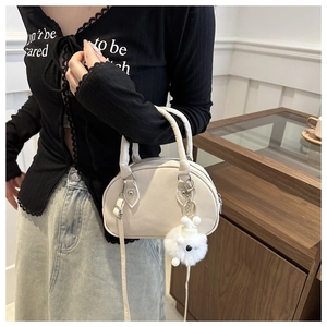 Beige Baseball-Handtasche im Detail mit abnehmbarem Gurt und weißem Plüschbär-Anhänger