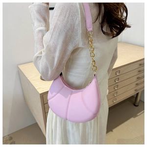 Pink crescent shoulder bag with gold chain strap shown on model in a modern interior