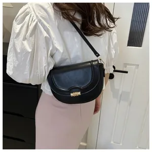 Elegant black leather saddle bag with gold metal clasp shown on a model's shoulder
