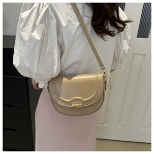 Close-up of beige saddle bag with gold metal clasp worn by model in a daily scene