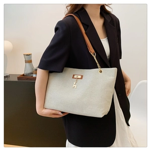 Detail of off-white canvas tote bag with brown leather and chain strap on a model