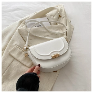 Detailed view of white leather saddle bag with gold metal ring clasp on a cream blazer