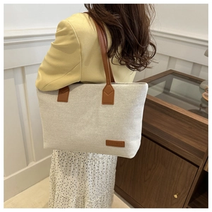 Shoulder view of a large canvas tote bag with brown straps and fashion leather label