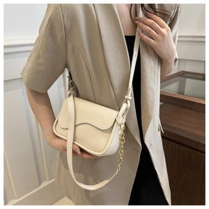 Fashionable off-white shoulder bag with wavy flap and gold chain detail on model