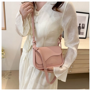 Pink matte leather saddle bag with adjustable strap worn by a model in a cozy interior