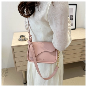 Detailed view of pink crossbody bag with curved flap, gold chain, and embossed logo