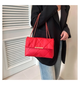 Macro detail of red quilted shoulder bag with gold chain strap and metal trim