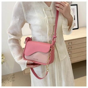 Detail of pink crossbody bag with wavy flap and gold chain strap held by a model
