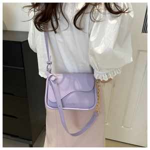 Detail of lavender crossbody bag with wavy flap design and gold chain link strap