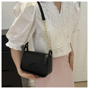 Detail of a black crossbody bag with wave flap and gold chain strap on a model