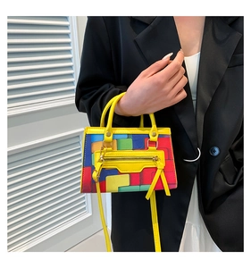 Detail of colorful pixel grid handbag with yellow leather handles and gold zippers