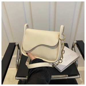 Detailed shot of cream crossbody bag with scalloped flap and gold chain on black chair