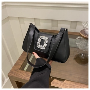 Detail of the rectangular rhinestone buckle on a black leather underarm shoulder bag