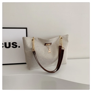 Detail of canvas tote bag with brown faux leather strap and golden deer pendant