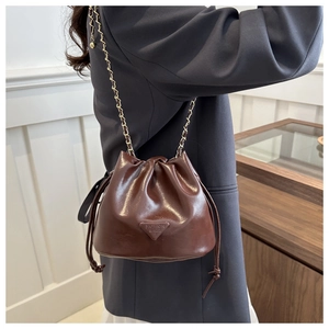 Close-up of brown leather bucket bag with gold chain strap and drawstring closure