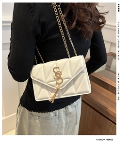 Detailed view of white quilted chain bag with gold S-lock and tassel charm on model