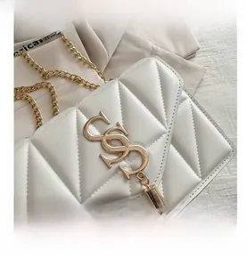 Detail of white quilted handbag with gold chain strap, metal logo, and tassel charm