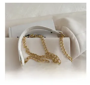 Detail of white leather shoulder strap with gold chain links and stitching on off-white fabric