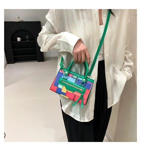 Close-up of vibrant color-blocked handbag with green leather handle and gold hardware