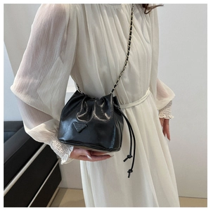 Detail of black drawstring bucket bag with triangular metal logo and chain strap