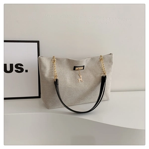 Detail of grey canvas tote bag featuring black straps and golden deer pendant decoration