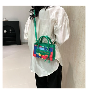 Model wearing a colorful geometric plaid handbag with green top handles and strap