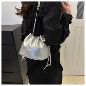 Detail of silver metallic drawstring bucket bag with gold chain strap and triangle plaque
