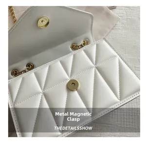 Detailed macro view of white quilted flap bag featuring golden magnetic snap closure
